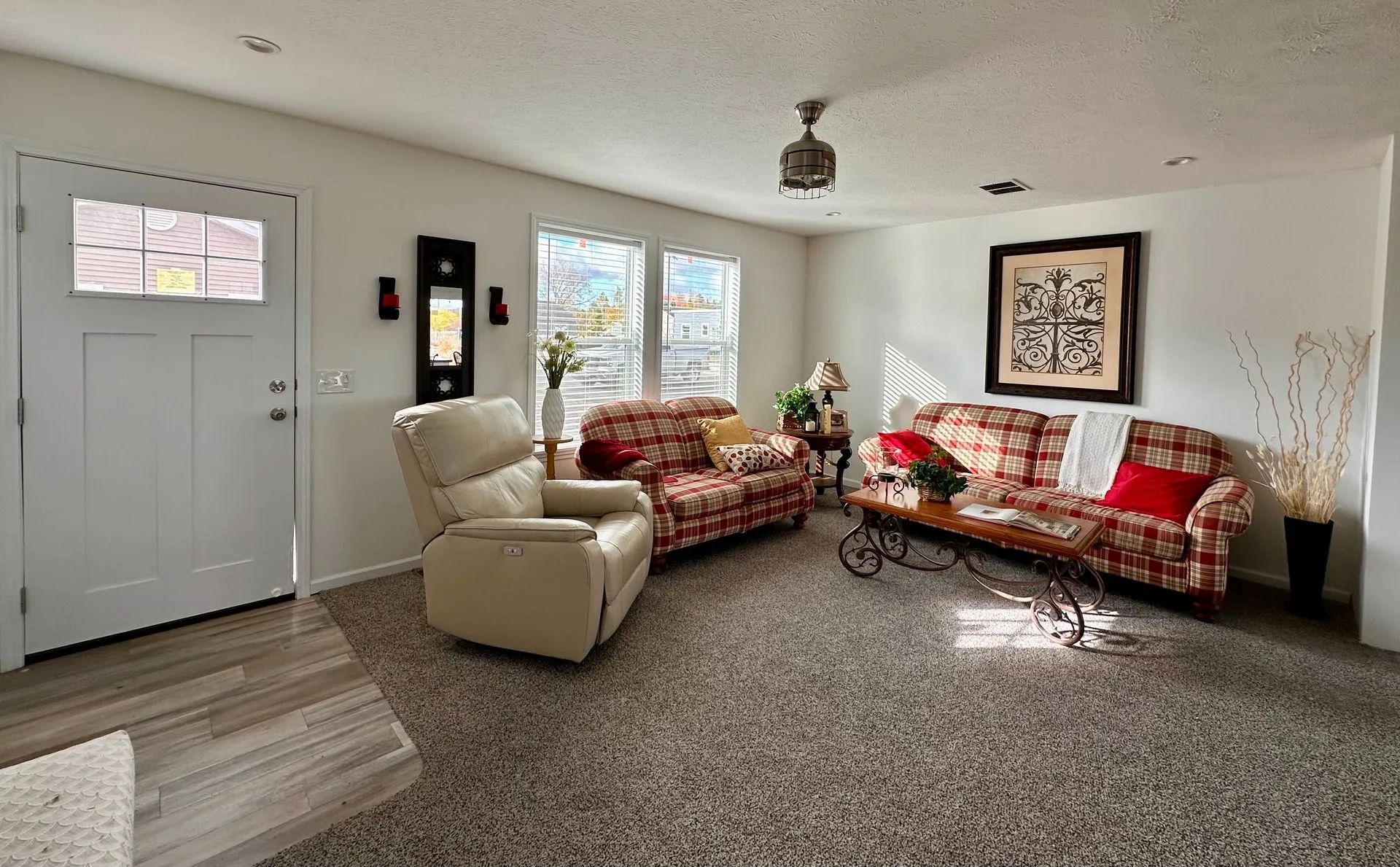 Living room with patterned sofas, beige recliner, large windows, and white walls