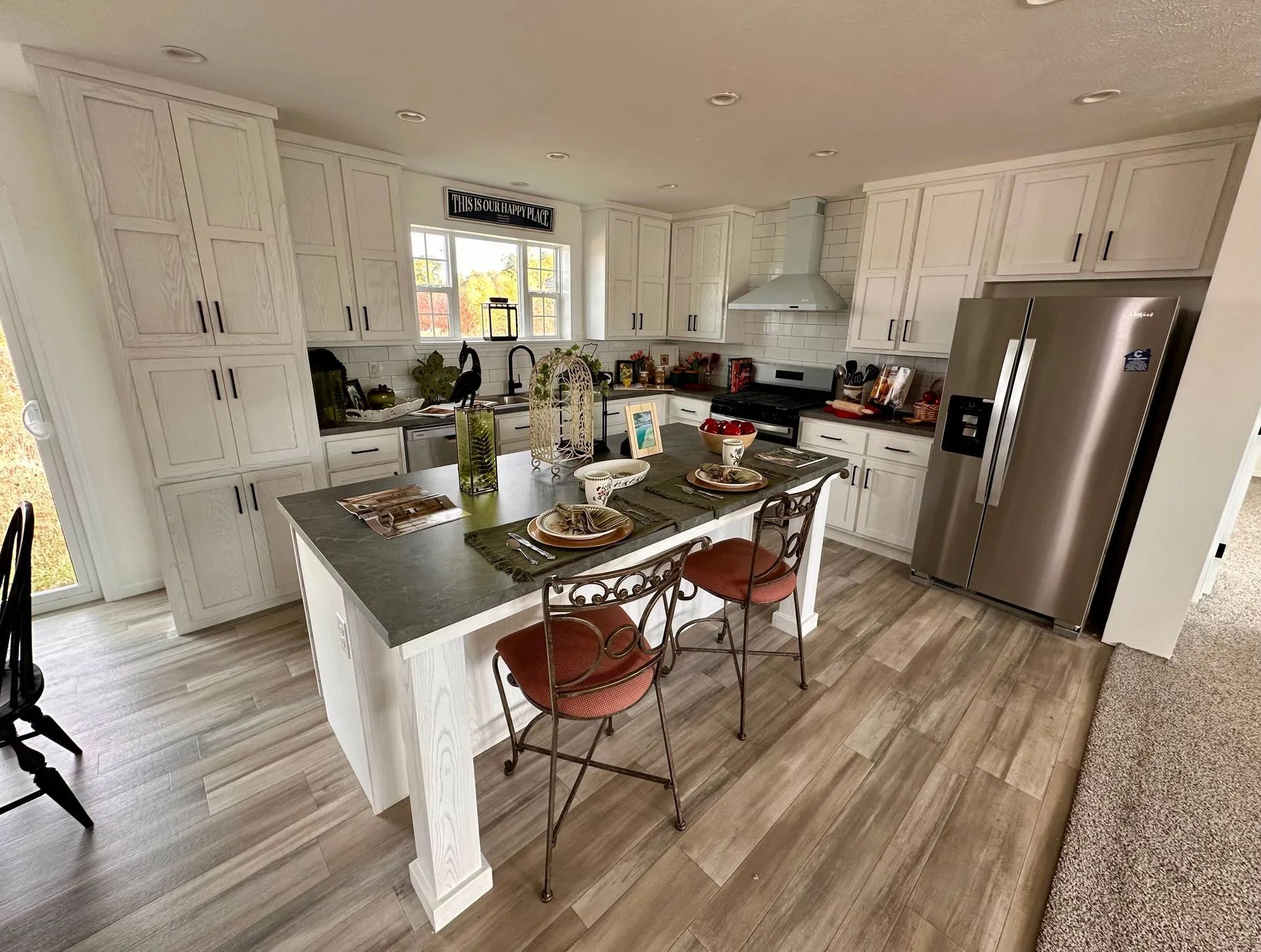 Bright modern kitchen with white cabinets, stainless fridge, island, and two red bar stools