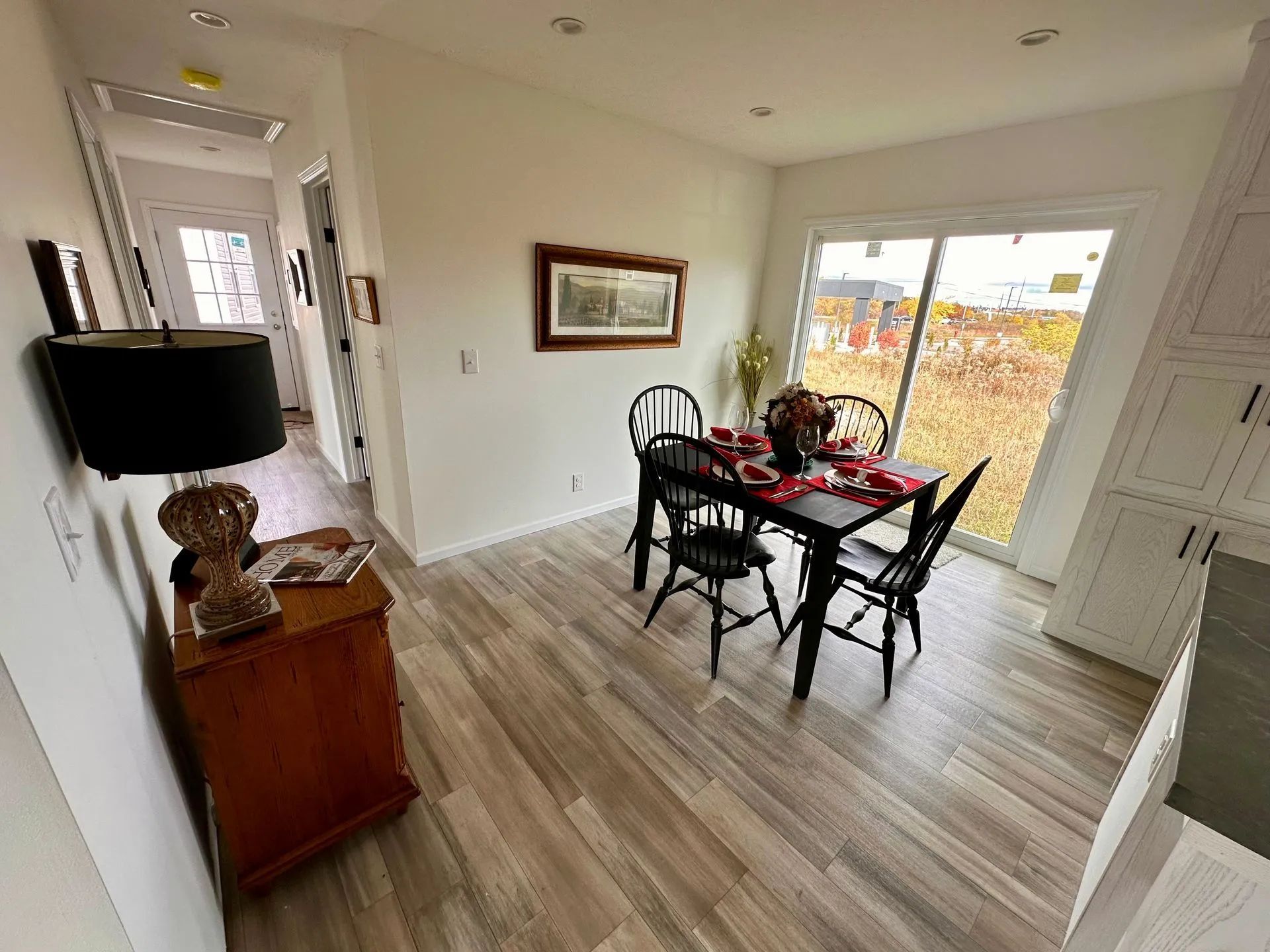Bright dining room with black table and chairs, red table setting, wood floors, and large window.