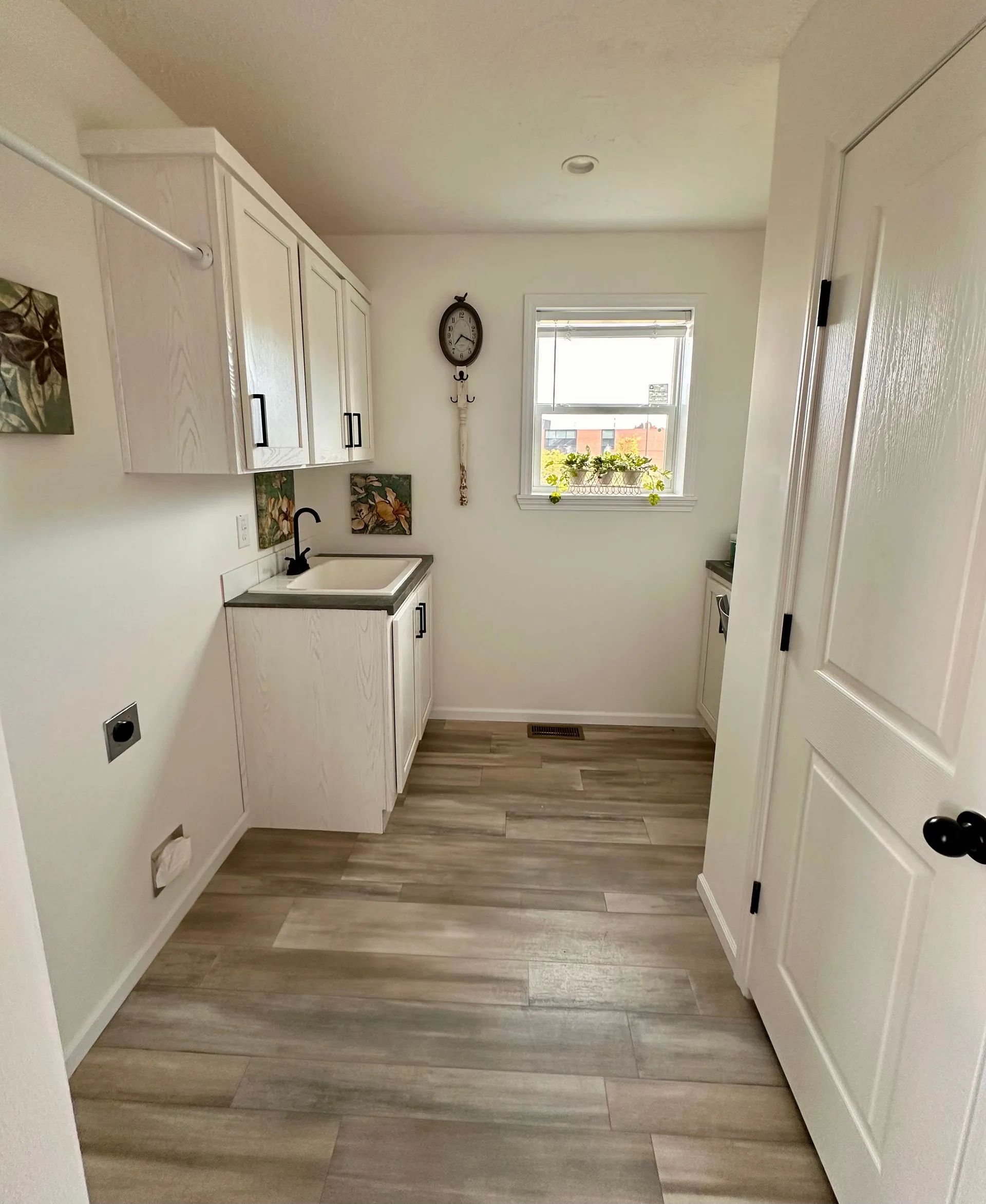 Narrow white kitchen hallway with wood-look flooring, cabinets on left, and a window at the end.