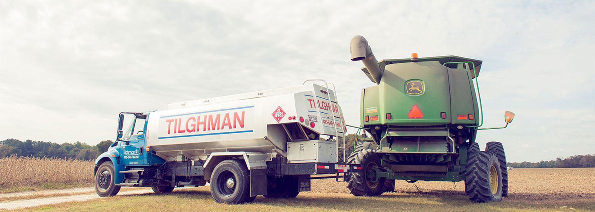 Blue and white fuel tanker beside a green combine harvester in a field