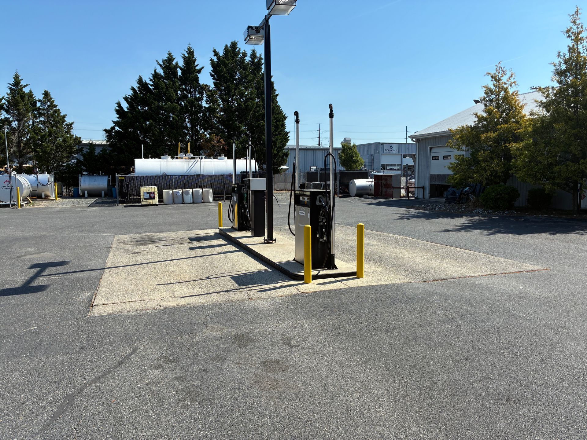 Outdoor parking area with a pump station, yellow bollards, and trees under a clear sky