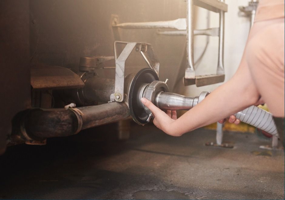 Hand using a hose to drain liquid from a car’s exhaust pipe under the vehicle