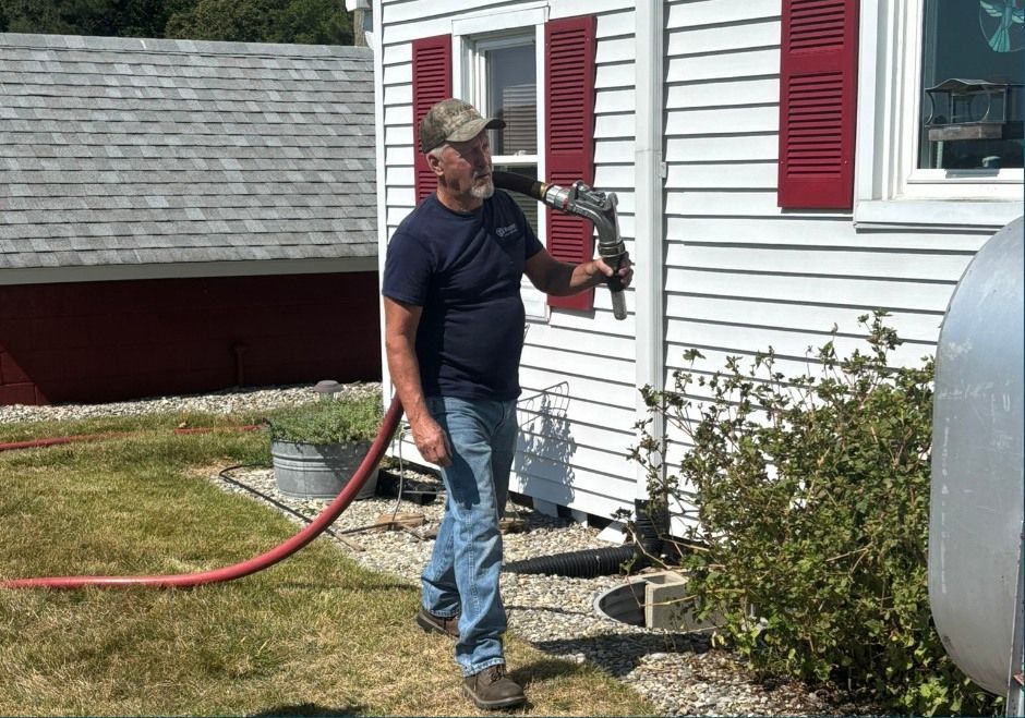 Man using a hedge trimmer beside a white house with red shutters and a red extension hose