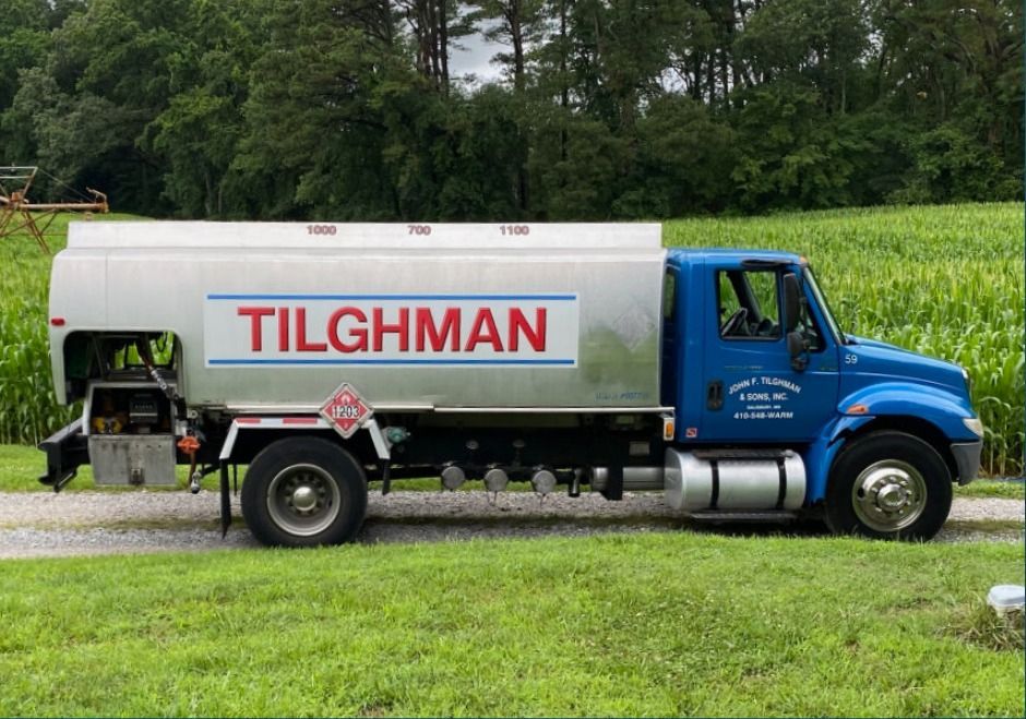 Blue Tilghman truck parked on grass beside a hedge and trees