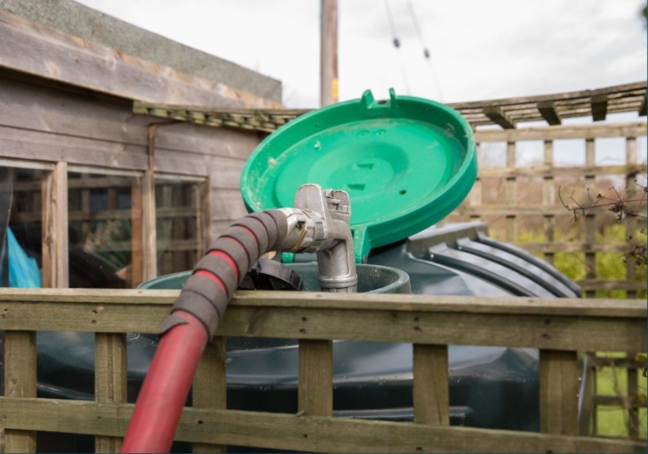 Red hose attached to a green tank lid behind a wooden fence outdoors