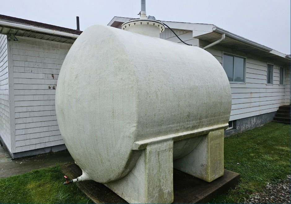 Large white cylindrical tank on concrete supports beside a house in a grassy yard