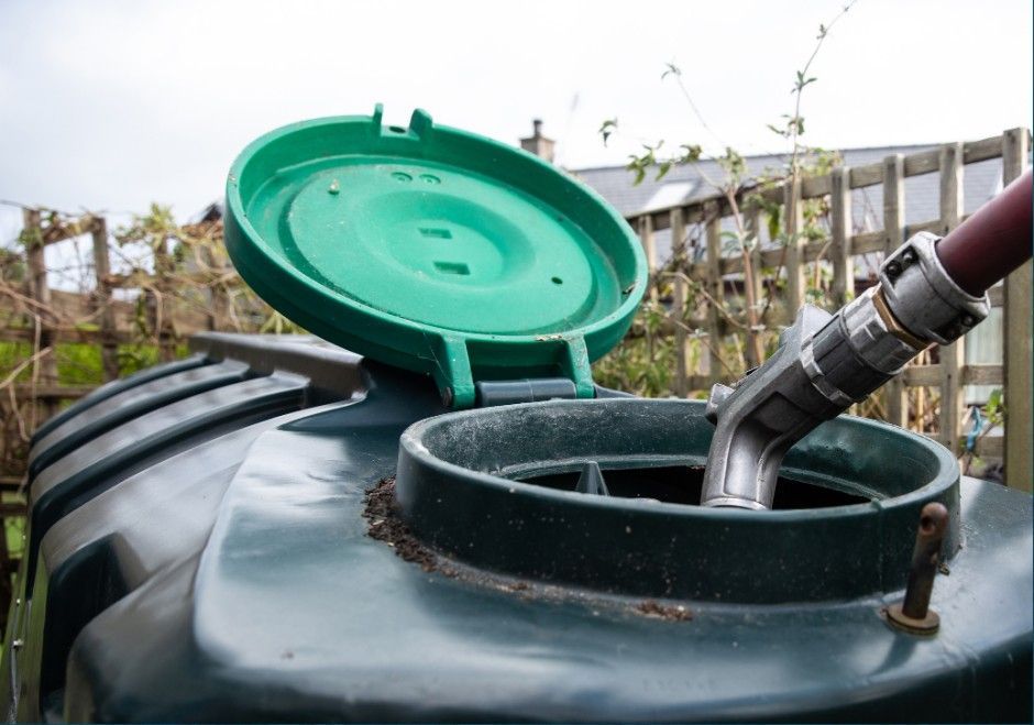 Green rainwater barrel with open lid and hose filling it outdoors
