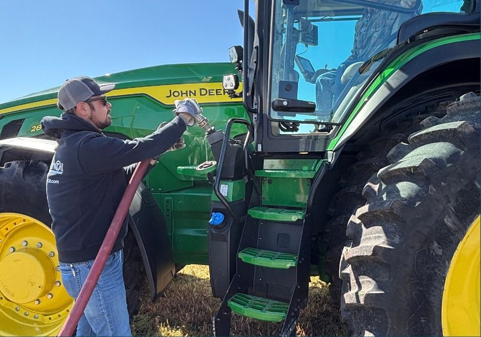 Man in a cap works beside a green John Deere tractor, handling a hose or cable in a field.