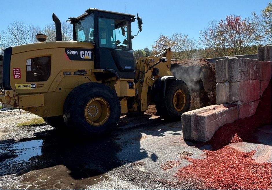 Yellow CAT loader pushing concrete blocks amid red debris on a sunny worksite
