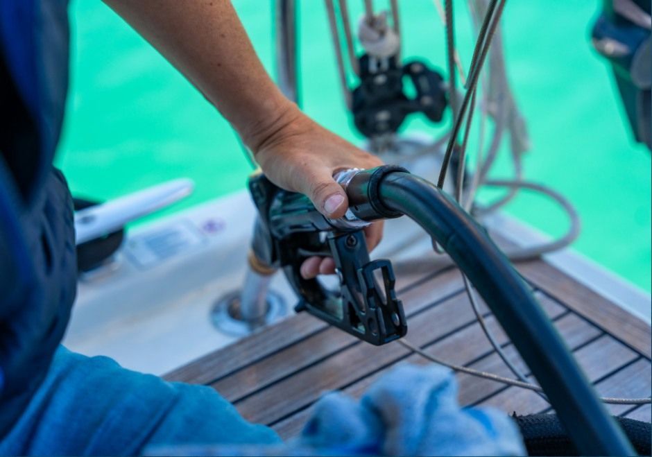 Hand holding a black hose near a wooden deck by turquoise water, with scuba gear in the background