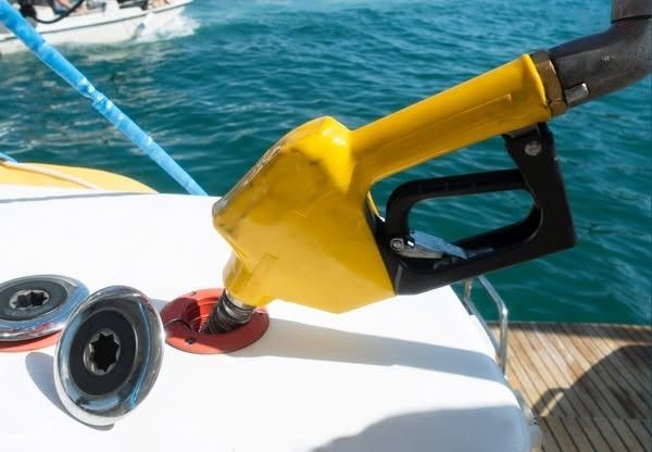 Yellow fuel nozzle filling a boat tank on deck by the water