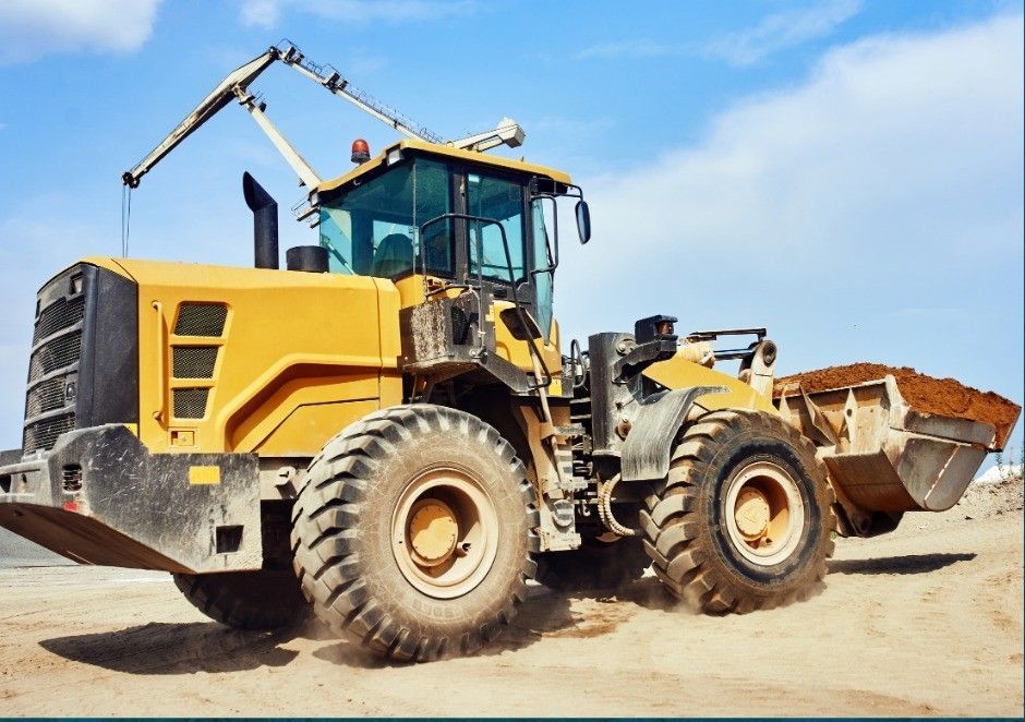 Yellow front loader with raised bucket on a dirt site under a blue sky