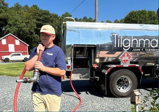 Man holding a hose beside a shiny tanker truck on a sunny day