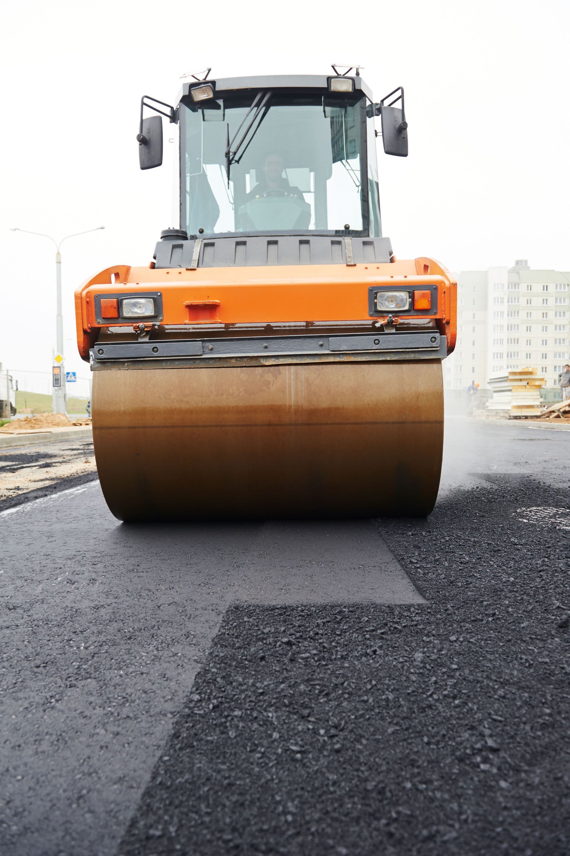 Orange road roller compacting freshly laid asphalt.