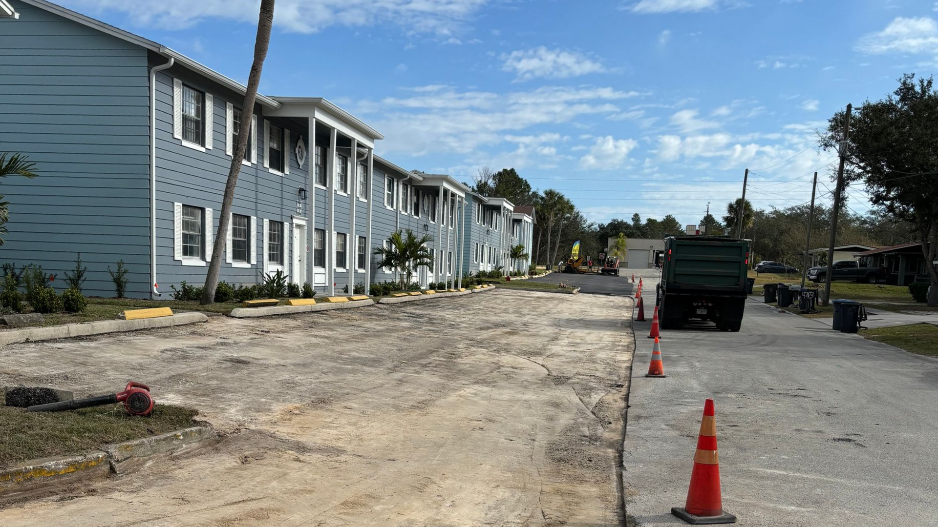 Construction site with blue apartment buildings, dirt road, truck, and cones.