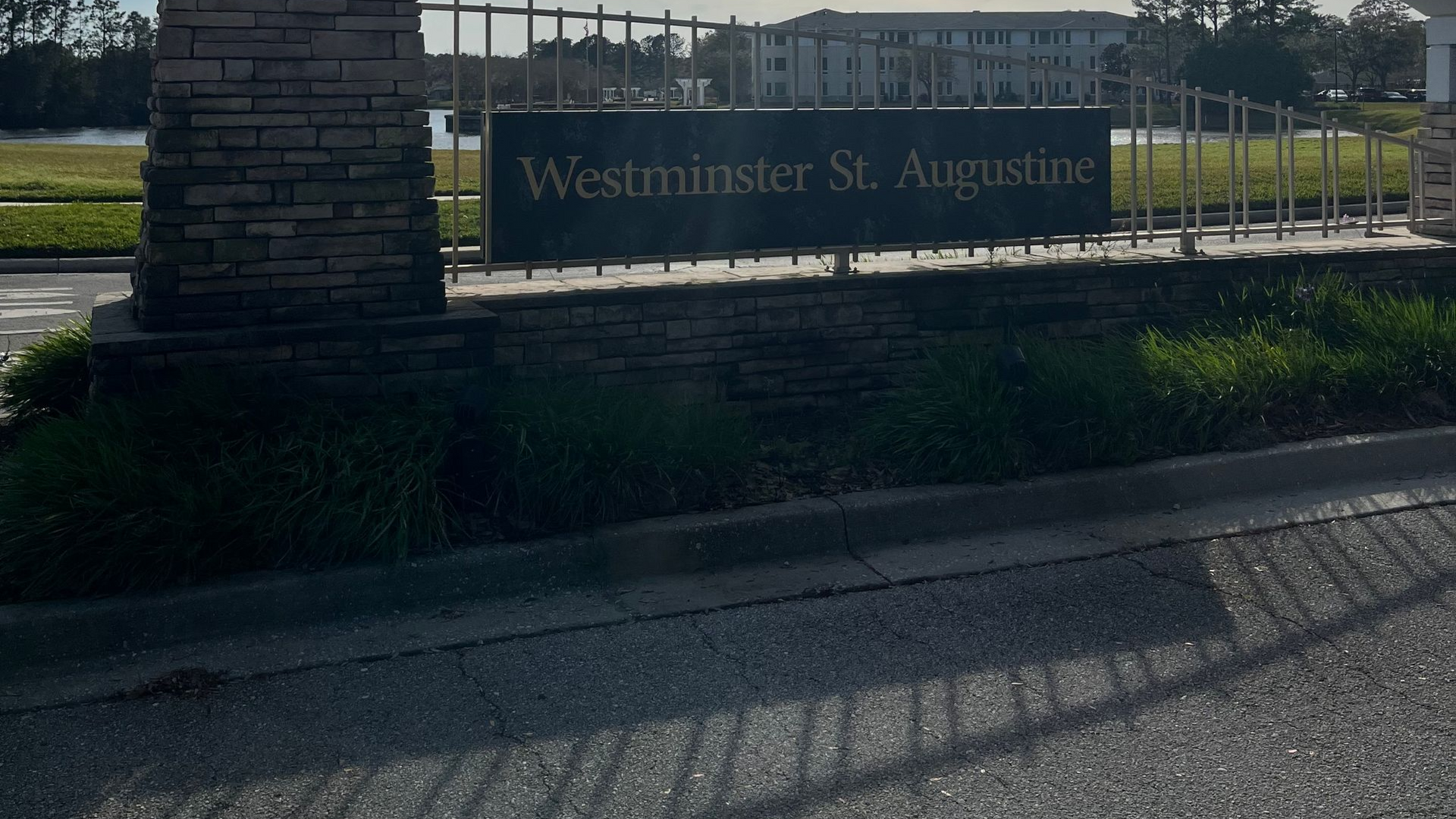Sign for Westminster St. Augustine, a senior living community, with a brick pillar, black text, and a wrought iron fence.