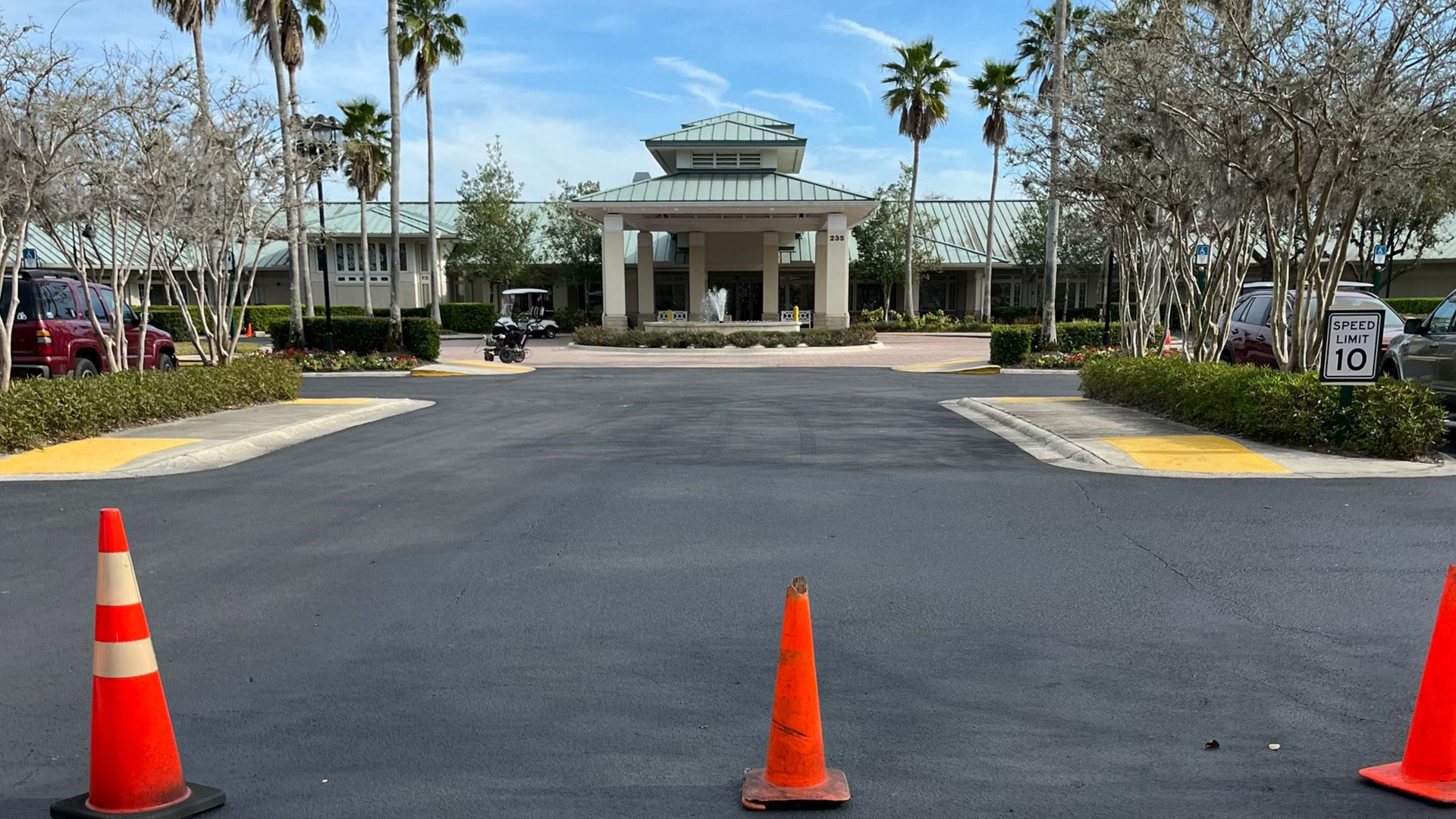 Entrance to a building with a canopy, lined with palm trees. Traffic cones are in the foreground.