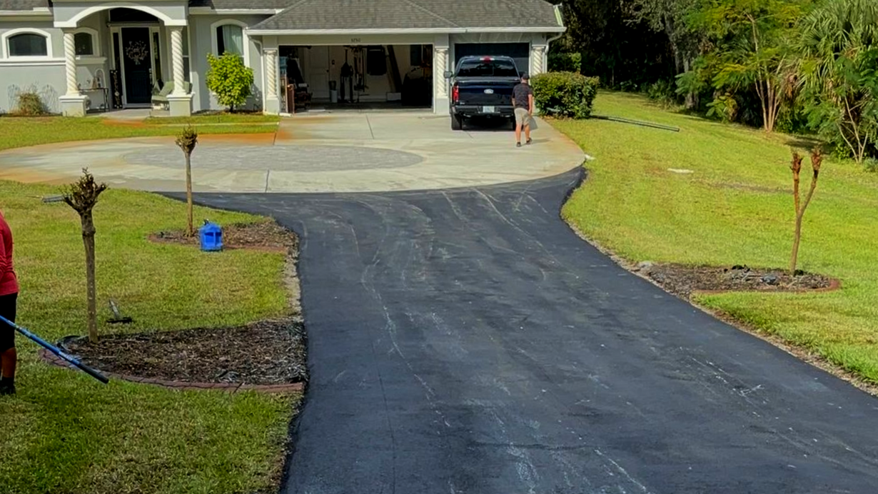 New asphalt driveway leading up to a house with a two-car garage. Workers on the lawn.