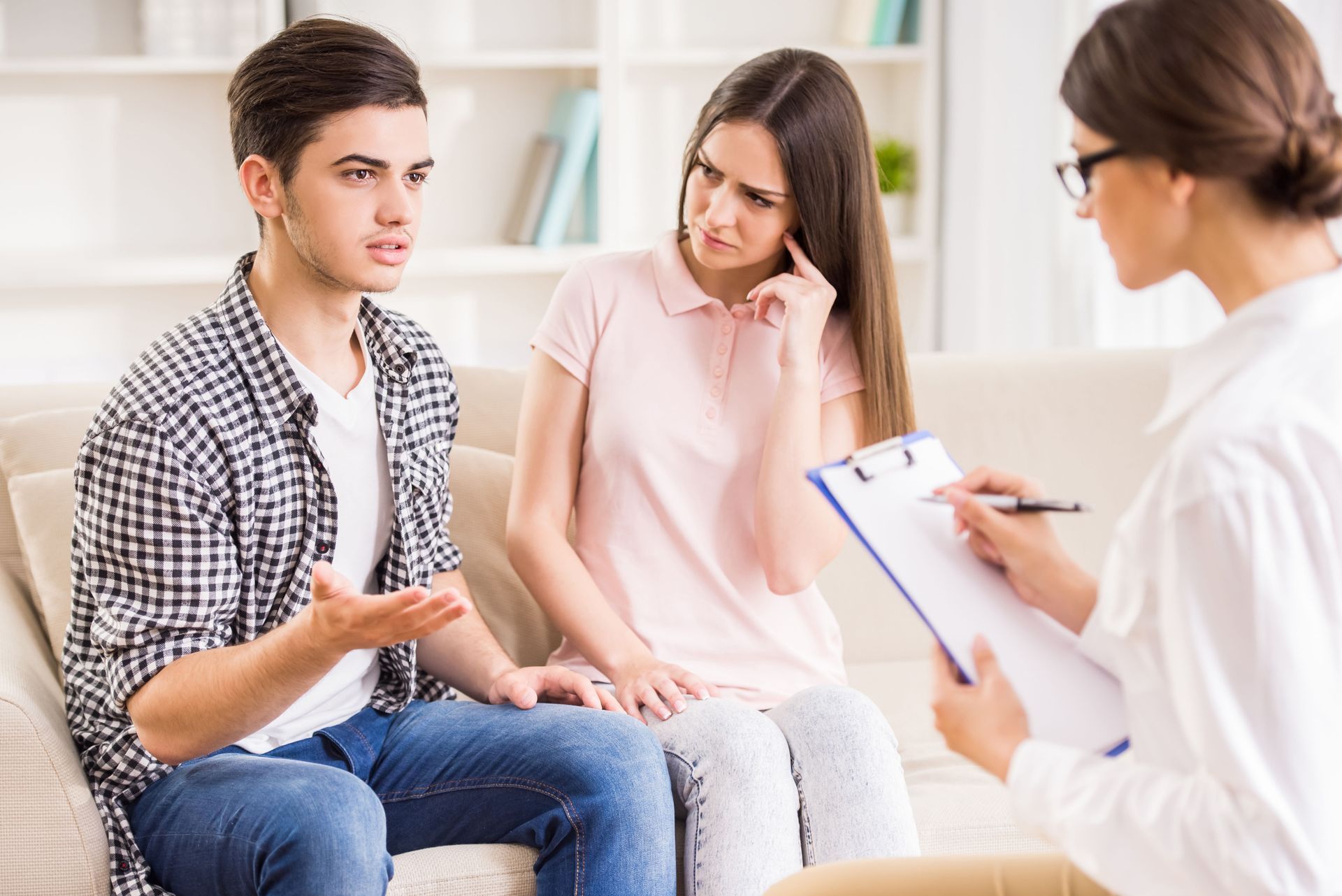 A young couple consults a therapist in a counseling session. The woman looks concerned while the man gestures.
