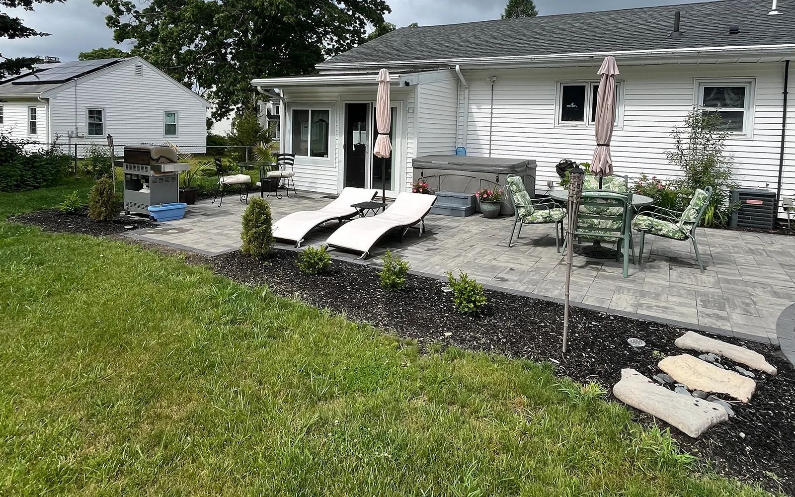 Backyard patio with lounge chairs, umbrella, grill, and dining set.