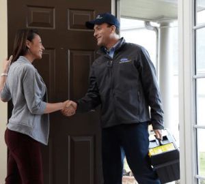 A woman shakes hands with a technician at a doorway. The technician holds a toolbox.