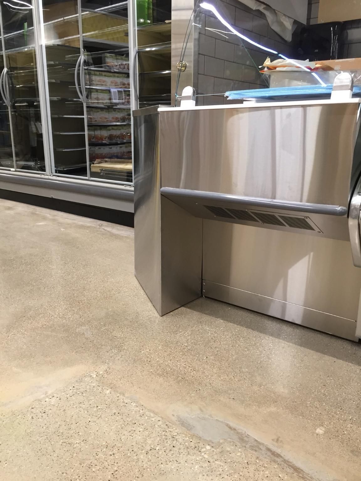 Stainless steel kiosk next to refrigerated display case on concrete floor.
