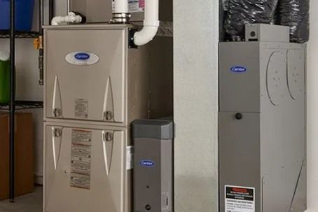 Two Carrier furnaces with white ductwork against a gray wall.