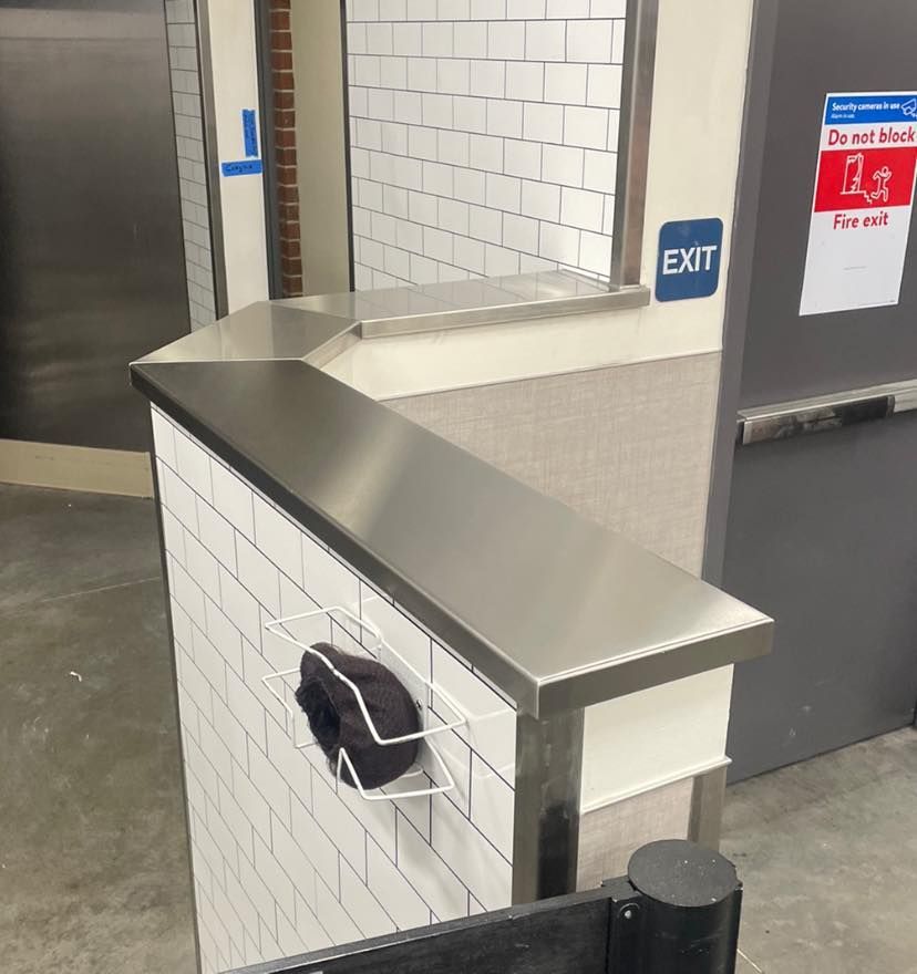 Stainless steel counter with a white-tiled wall and a black hat in a wire basket. 