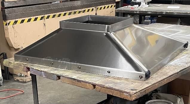 Stainless steel commercial kitchen hood on a workbench.