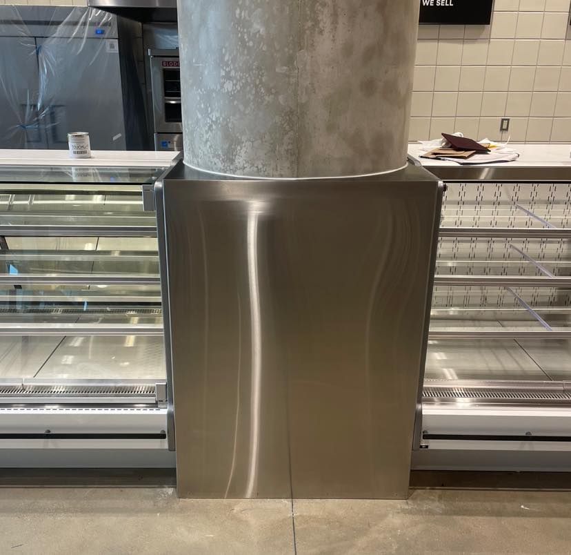 Stainless steel counter with a support column in front of display cases.