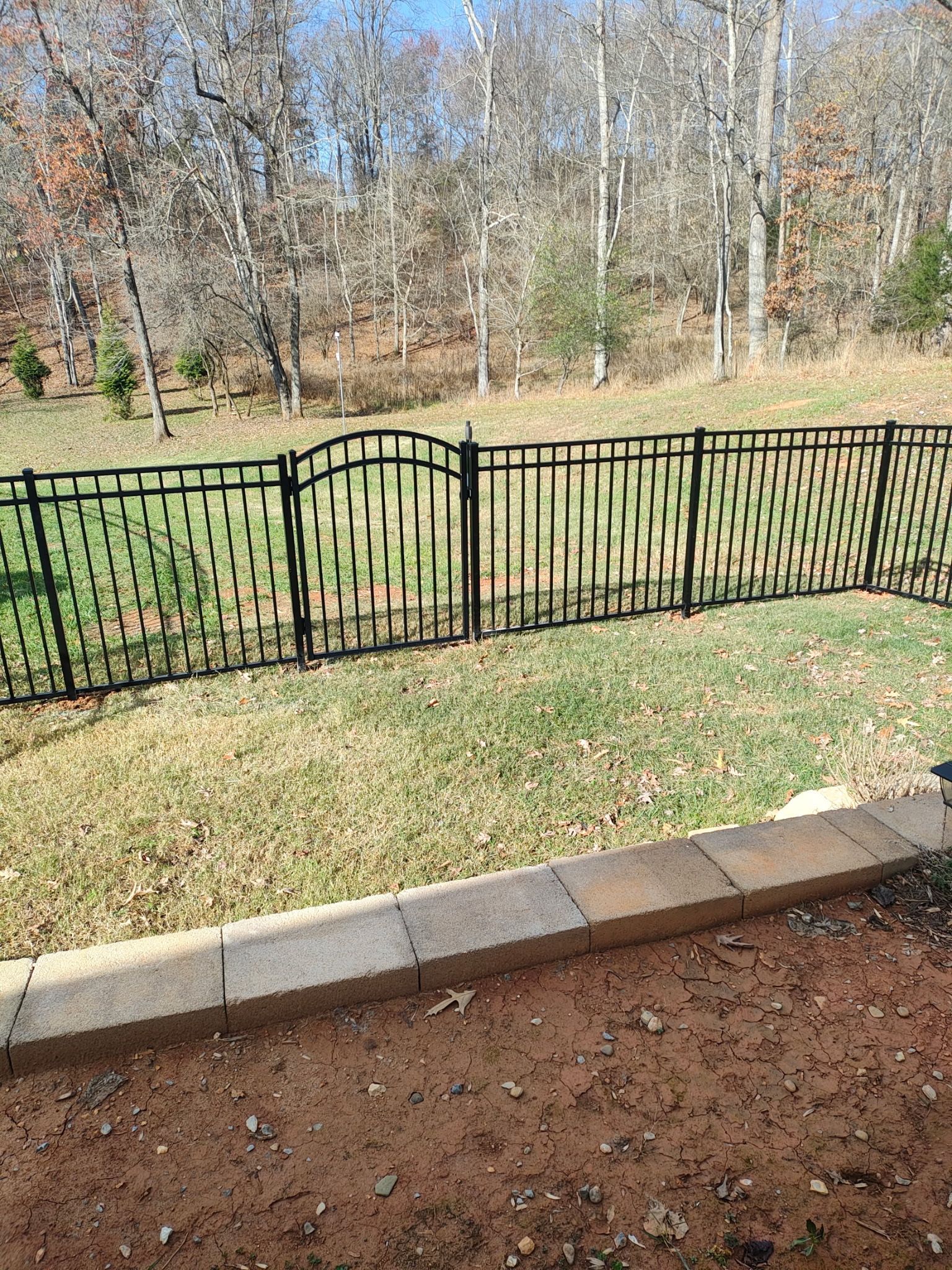 Black metal fence along a grassy yard with trees in the background and a stone border in front