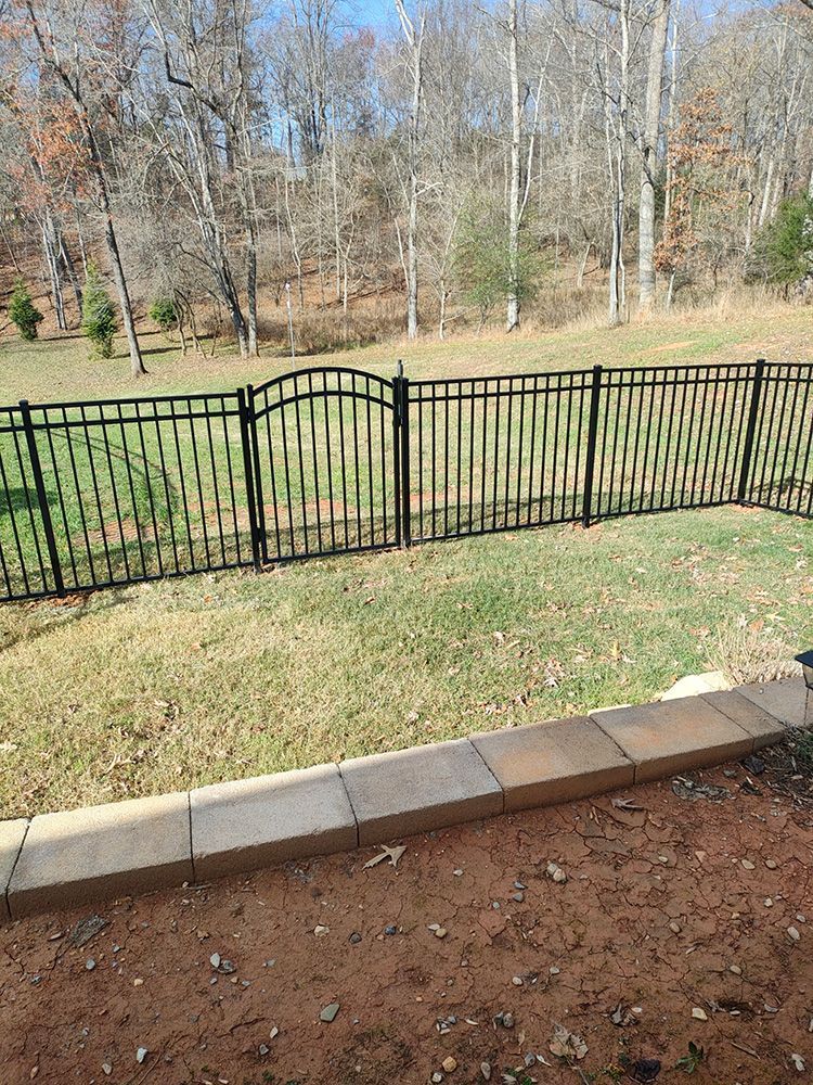 A wooden fence surrounds a lush green field with trees in the background