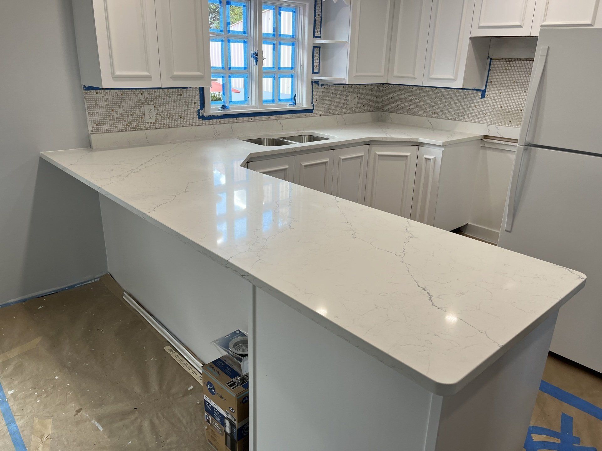 A kitchen under construction with white cabinets and a white countertop