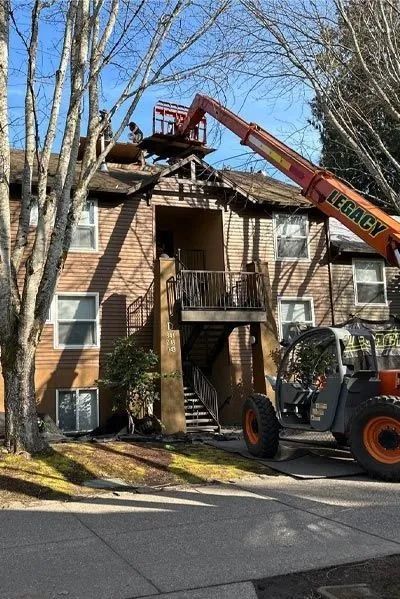 Workers on a lift repairing the roof of a multi-story wood-sided apartment building.
