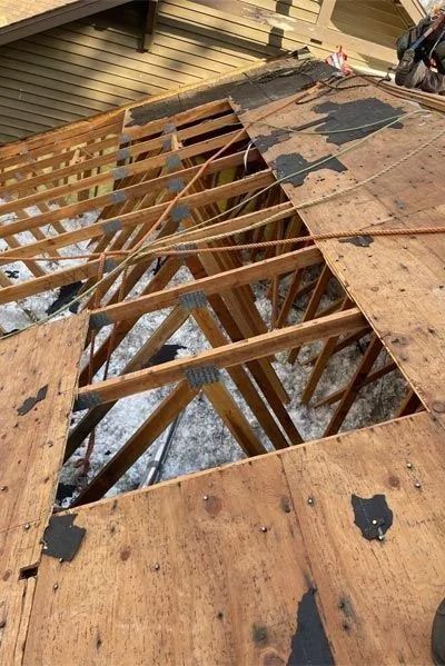 View of roof under construction, plywood sheathing with sections removed, showing trusses and insulation.
