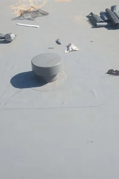 Gray roof with a vent, surrounded by tools and debris.