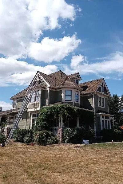 Large two-story house with a ladder leaning against it on a sunny day.