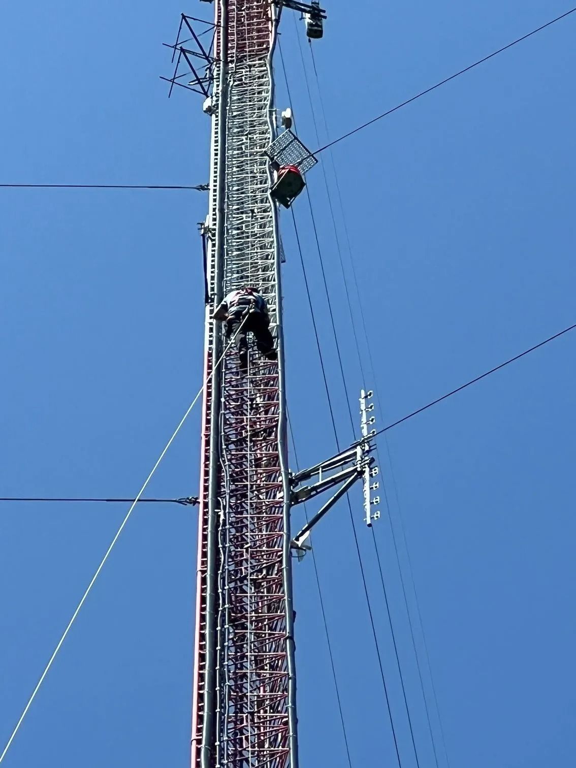 Man climbing a tall communications tower on a sunny day.