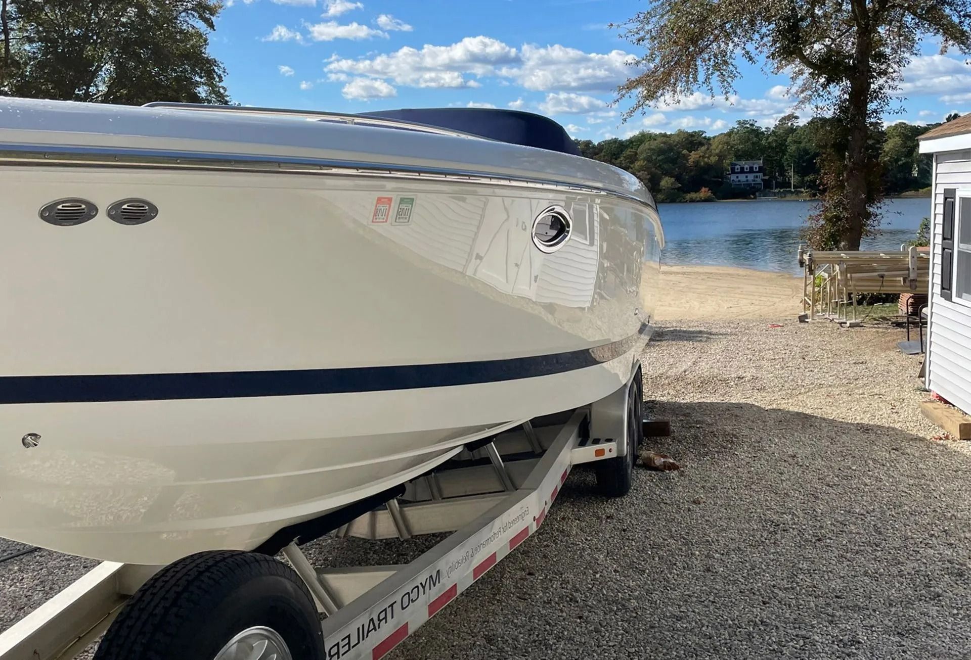 White boat on a trailer, next to a sandy shore with a lake, under a blue sky.
