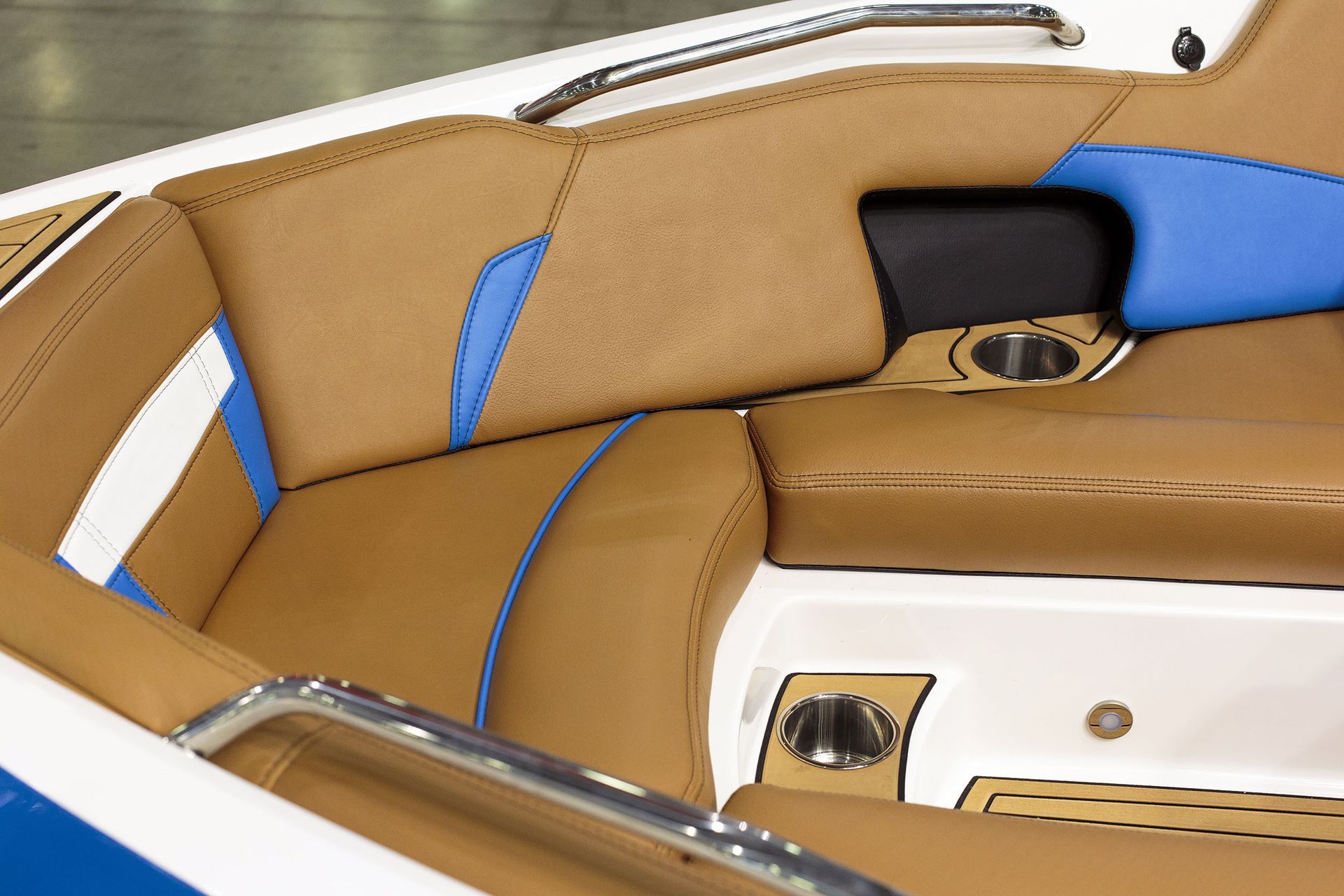 Interior of a boat with tan and white seating, wood floors, and a steering wheel, overlooking a body of water.