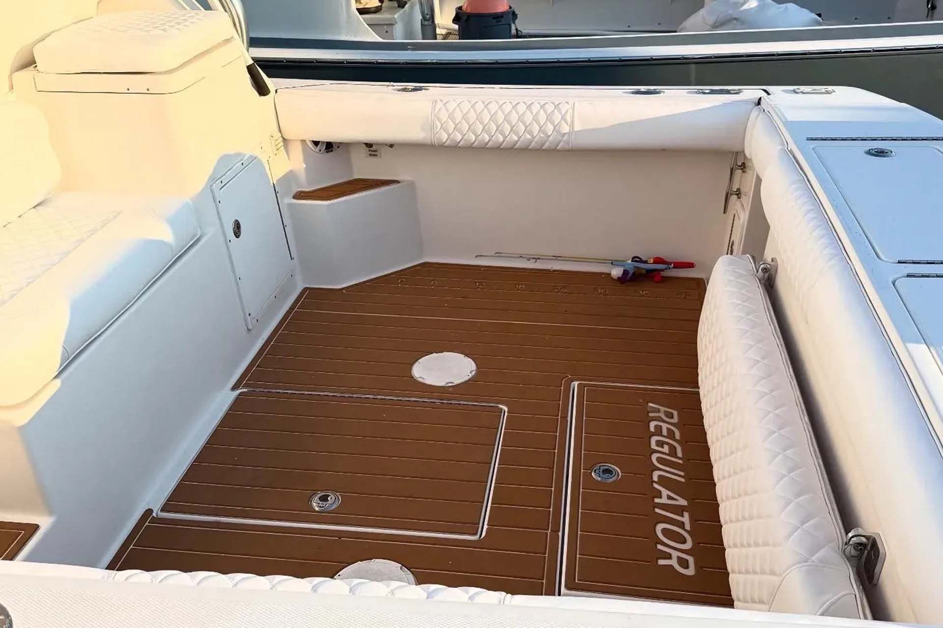 The rear cockpit of a white Regulator boat featuring brown wood-grain decking, white quilted seating, and storage hatches.