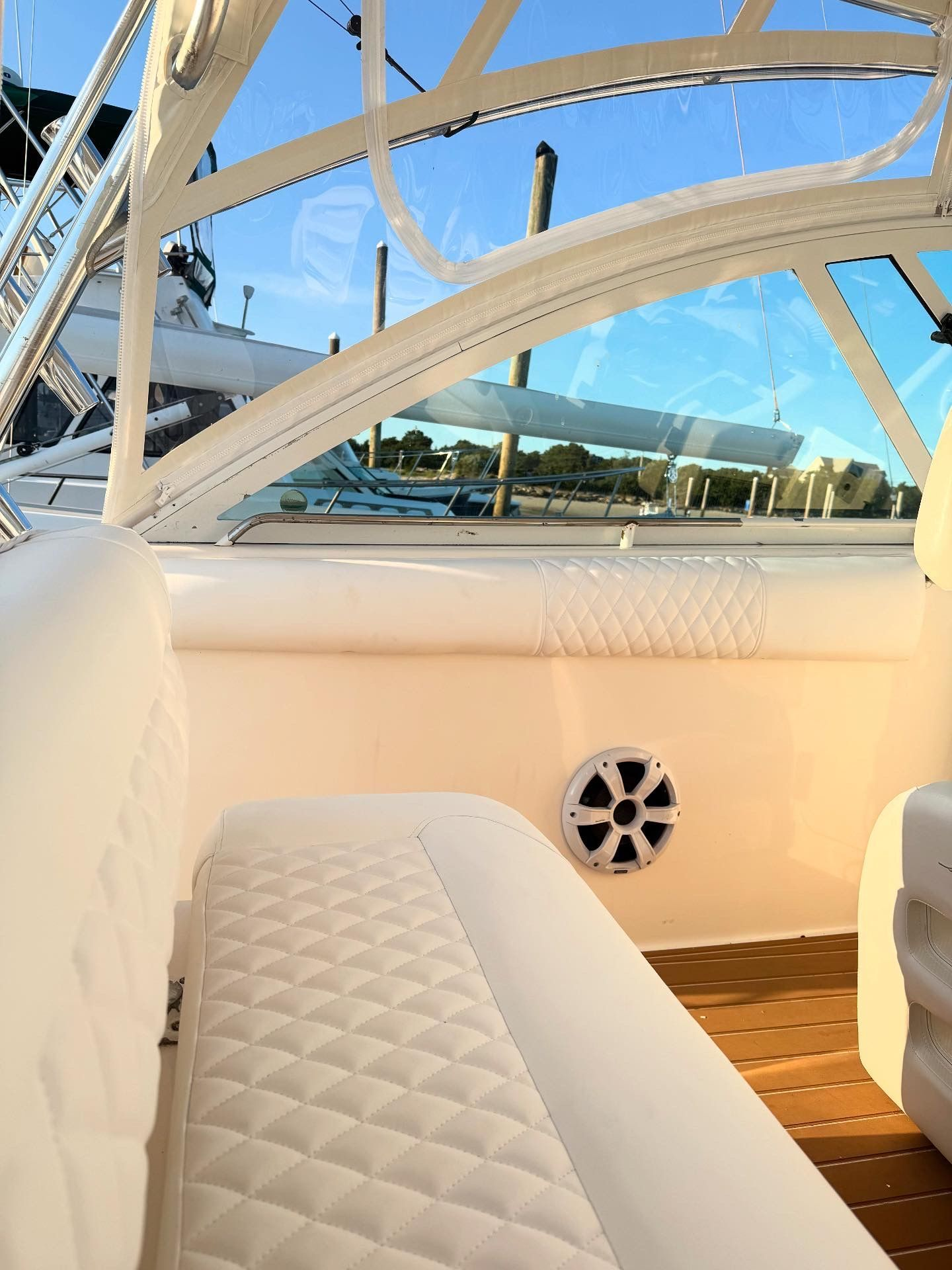 Interior of a white boat with diamond-stitched seating, a clear windshield, and a speaker.
