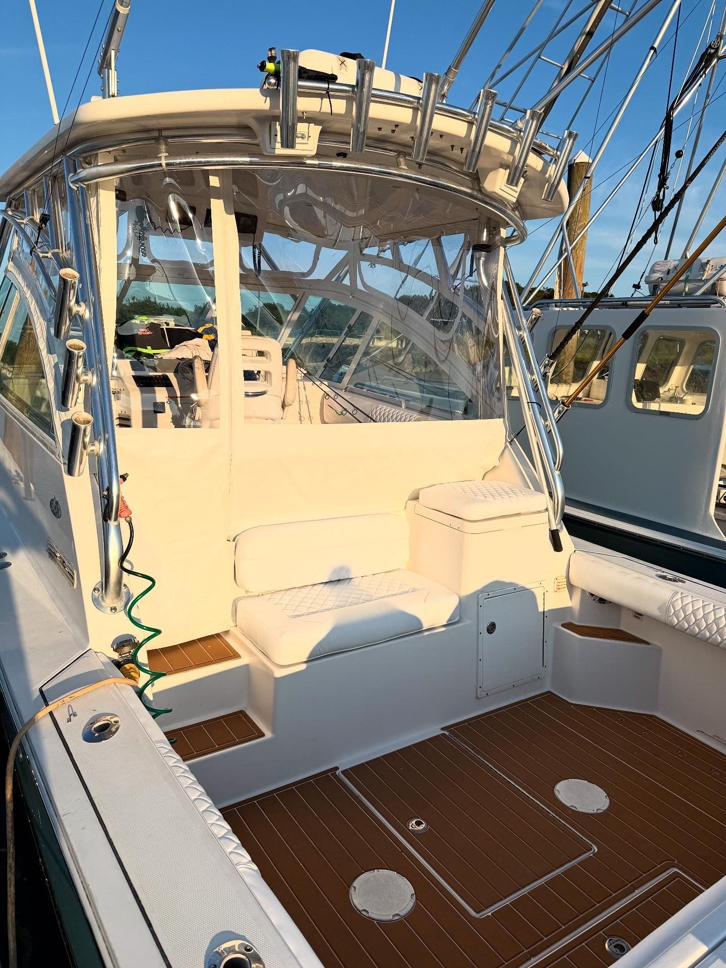 Back of a white fishing boat with brown decking, clear side panels, and fishing rods.