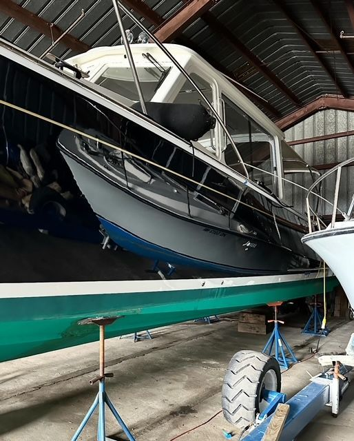 Gray and white cabin cruiser boat in a dry dock, supported by stands, inside a warehouse.