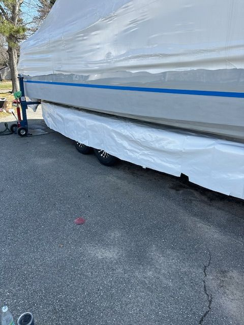 Boat covered in white shrink wrap on a trailer. The boat is silver with a blue stripe.