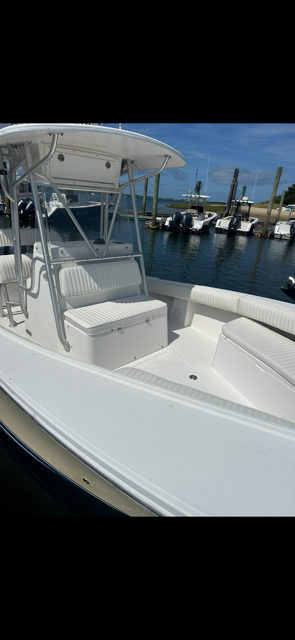 White boat docked at a marina with other boats and blue water under a sunny sky.