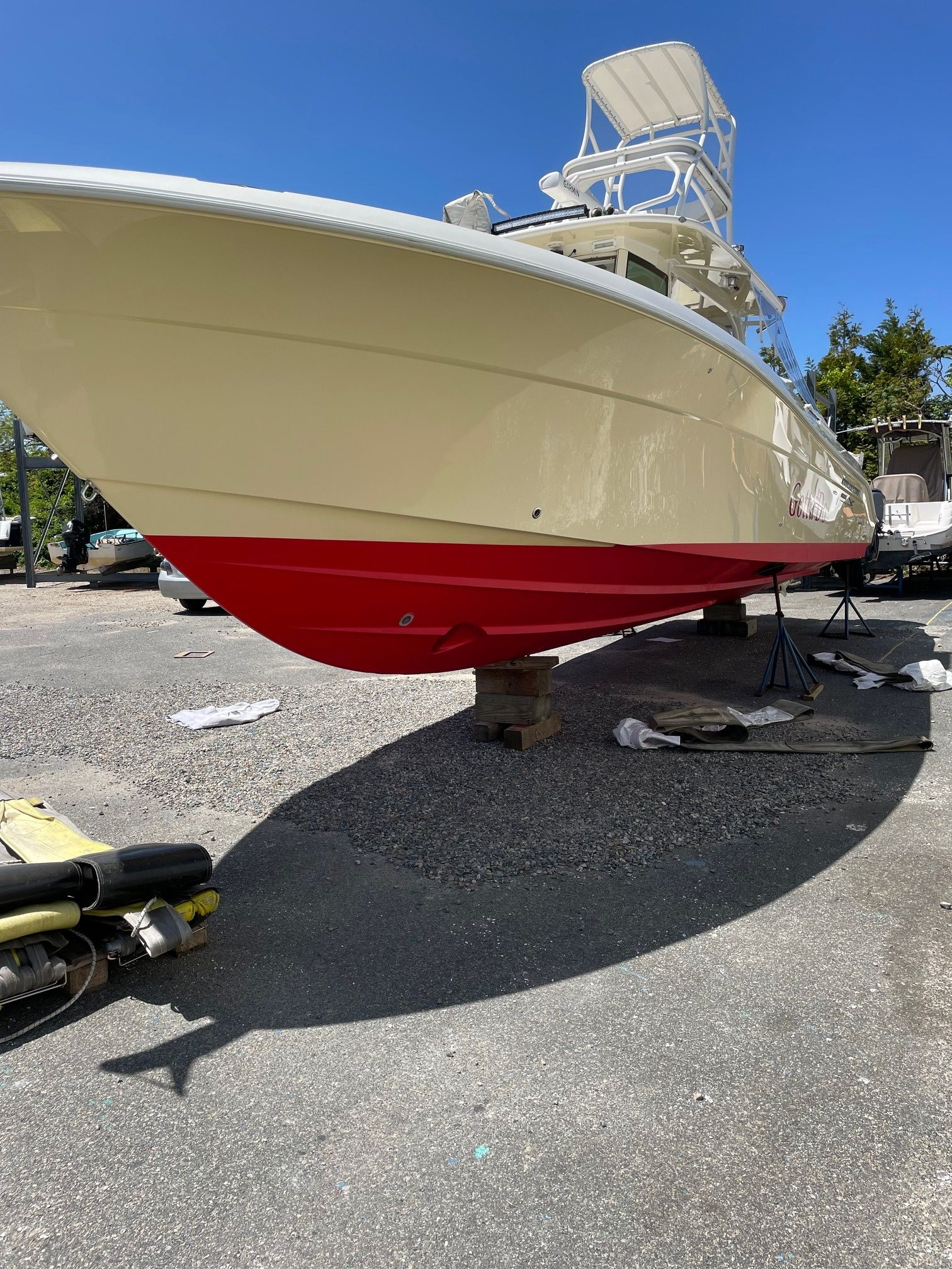 Beige and red motorboat on dry dock, under sunny sky.