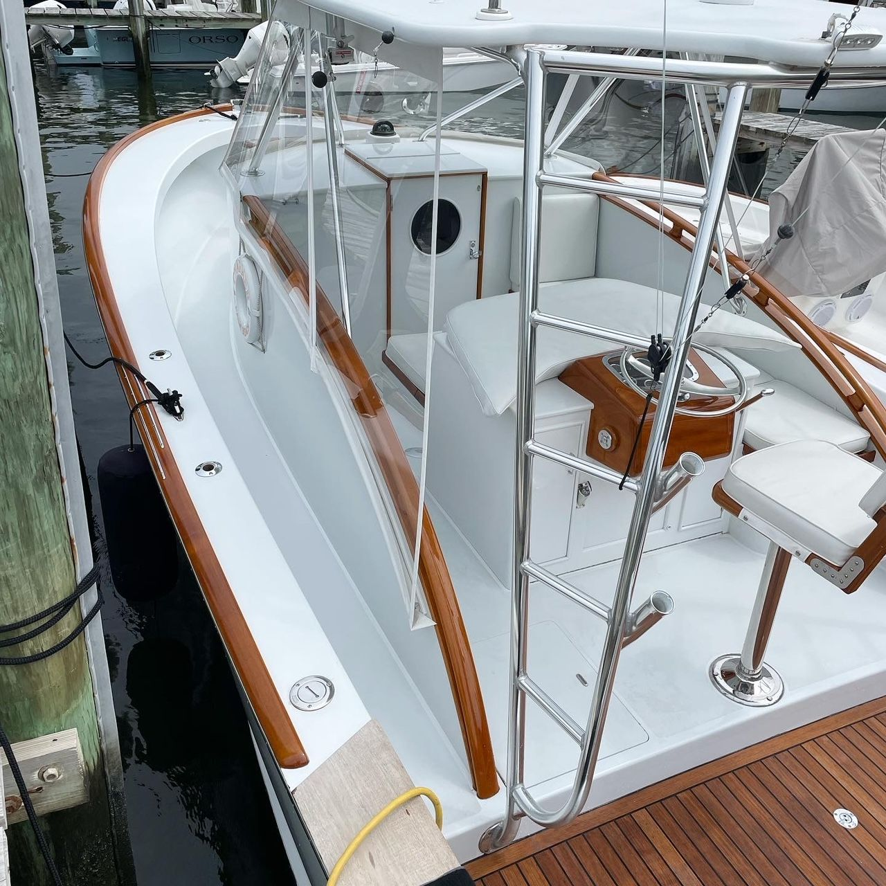 White and wood-trimmed boat docked at a marina, with clear plastic enclosure and wooden deck.