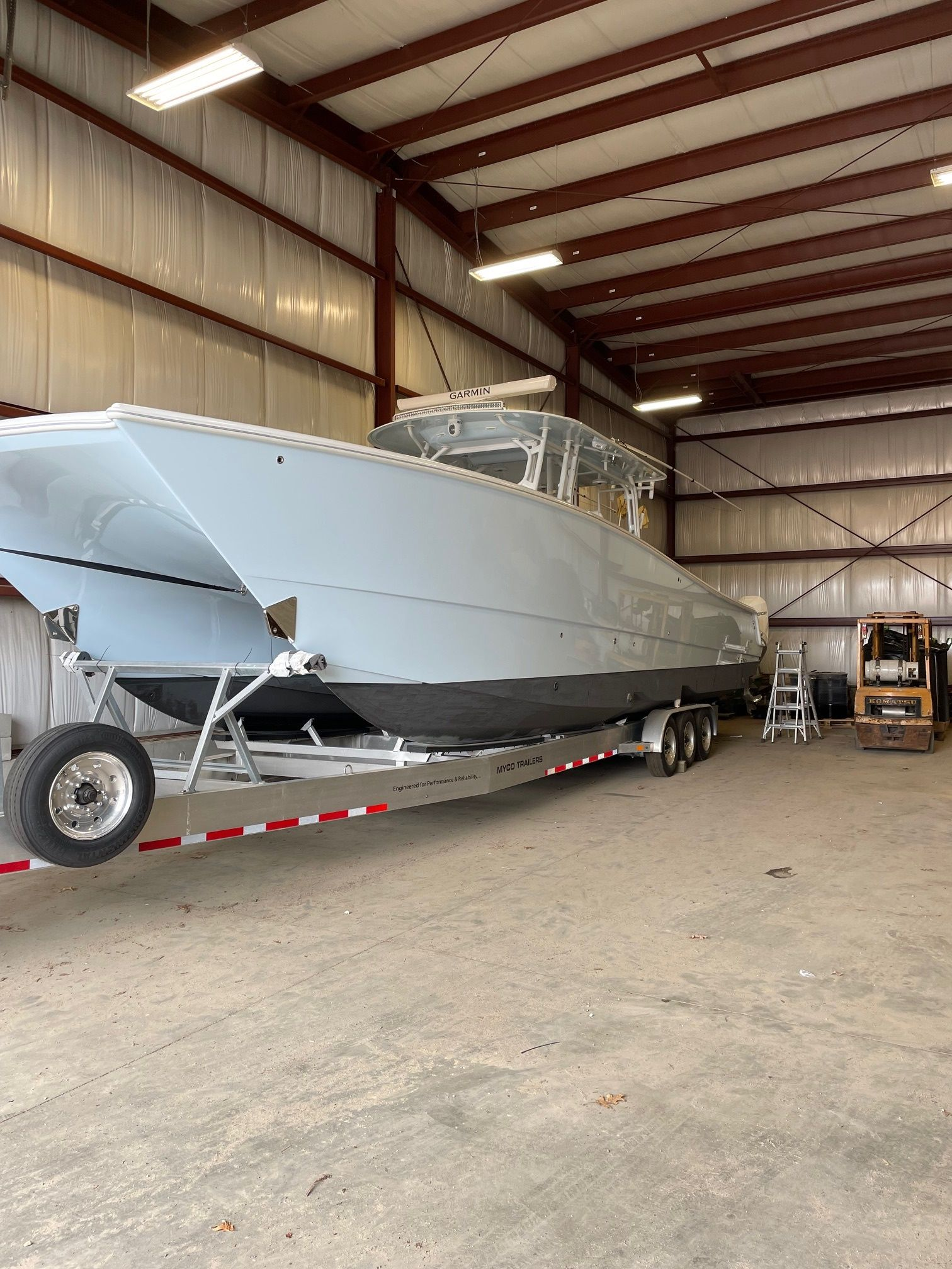 Large gray boat on a trailer inside a warehouse, with a forklift visible.